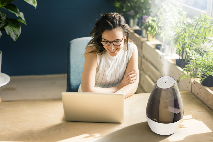 Woman sitting at her home office desk surrounded by houseplants with steam coming out of L100 humidifier