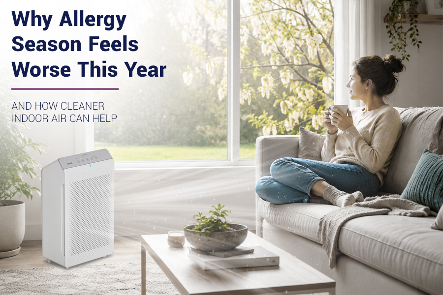 Woman relaxing on a sofa in a bright, modern living room with sunlight streaming through a window and spring blossoms outside, symbolizing indoor comfort during allergy season.