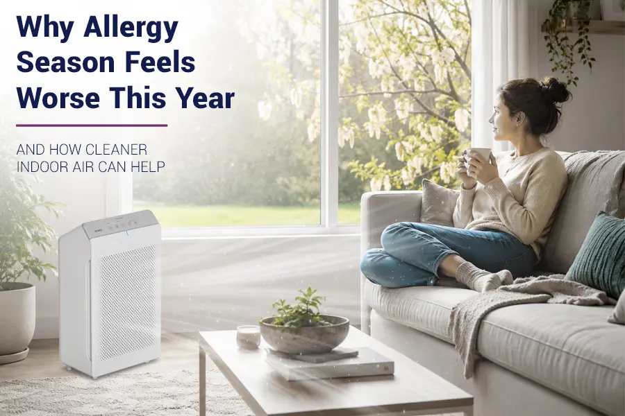Woman relaxing on a sofa in a bright, modern living room with sunlight streaming through a window and spring blossoms outside, symbolizing indoor comfort during allergy season.